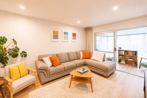 Una sala moderna con un sofá seccional beige, una mesita de centro de madera, un sillón amarillo y una estantería.