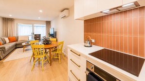Una cocina moderna con estufa integrada, mesa de comedor de madera con sillas y una sala de estar con sofá y televisor.