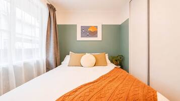 A hotel room with a bed, a window with curtains, a wall-mounted artwork, and a bedside plant.