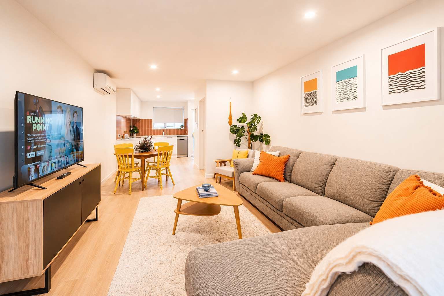 A modern living room with a flat-screen TV, a sofa, a coffee table, and a dining area with chairs.