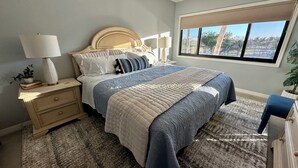 A bedroom with a bed, nightstands, a window, and a view of the outdoors. - Bayfront Condo: Your Sunset Paradise on Fort Myers Beach (Fort Myers Beach)