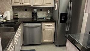 A modern kitchen with stainless steel appliances, light wood cabinetry, and a black countertop. - Bayfront Condo: Your Sunset Paradise on Fort Myers Beach (Fort Myers Beach)