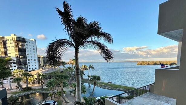 A view of a residential area with a swimming pool, palm trees, and a body of water. - Bayfront Condo: Your Sunset Paradise on Fort Myers Beach (Fort Myers Beach)