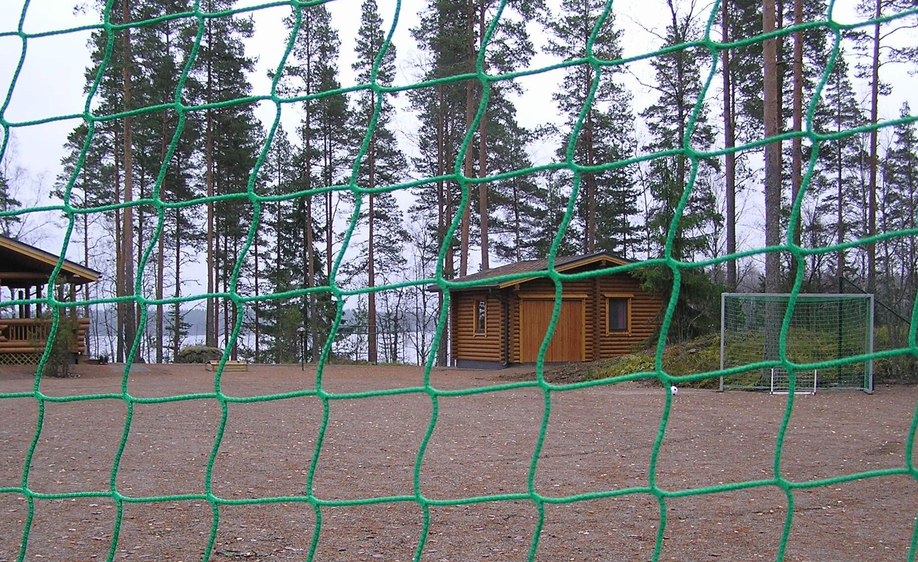 Una cabaña rodeada por una zona verde con mosquiteras y un bosque de fondo.