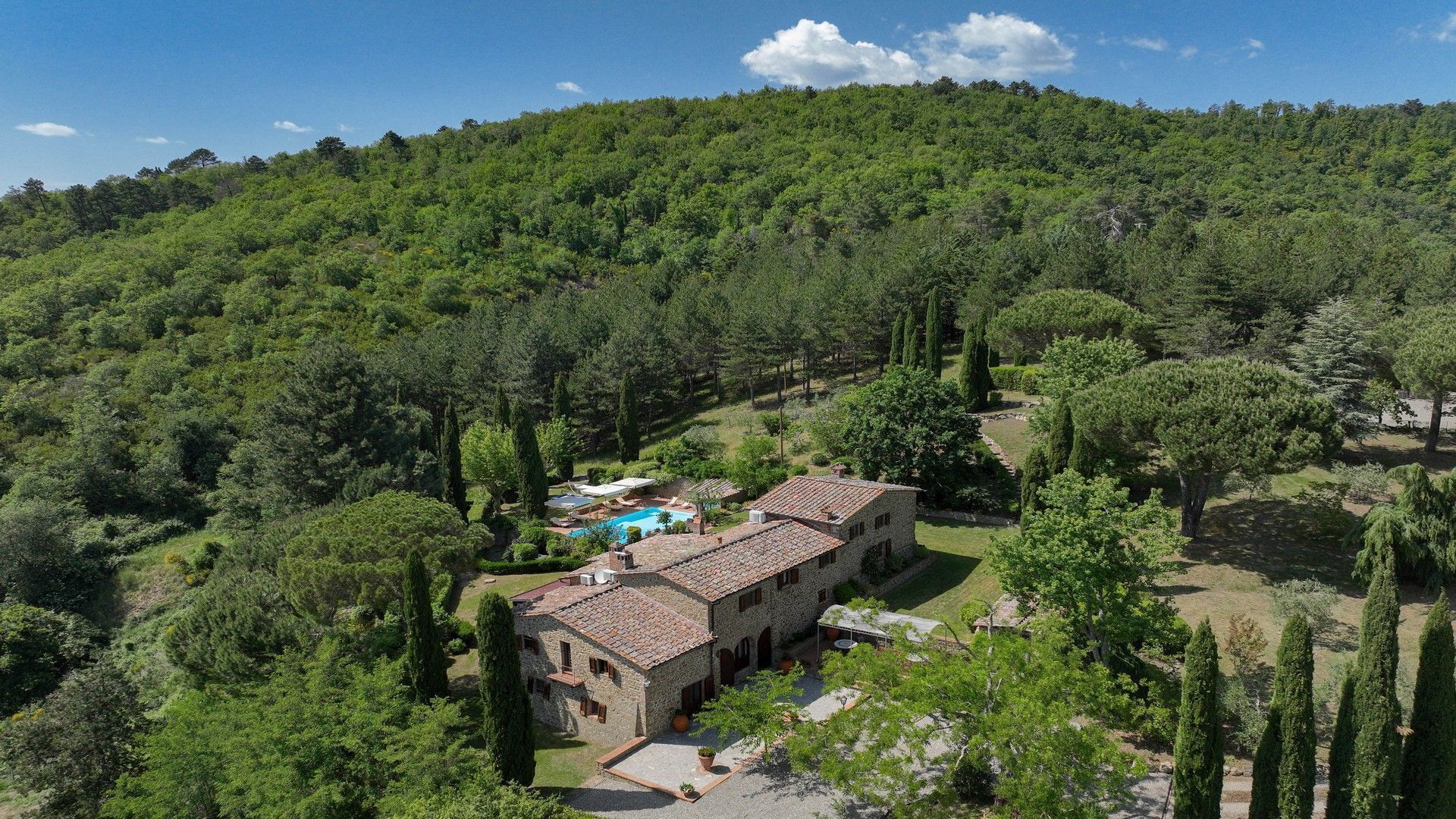 Une villa en pierre dotée d’une piscine et d’un jardin aménagé en terrasses, entourée d’une forêt dense.