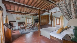 A rustic bedroom with a wooden ceiling, a bed with a green lamp, and a desk with a chair.