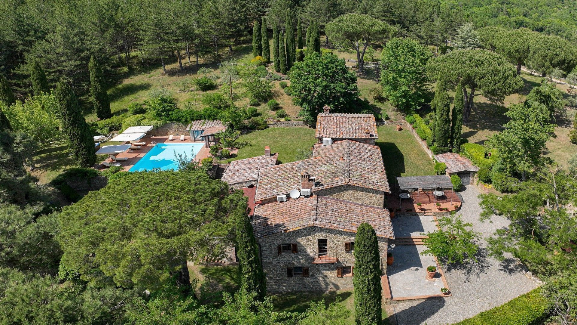 Uma villa de pedra com piscina, rodeada por vegetação exuberante e árvores altas.