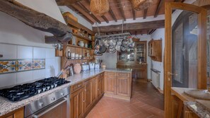 A rustic kitchen with wooden cabinets, a gas stove, and hanging pots.