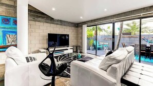 A modern living room with a white sofa, a black chair, a TV, and a glass door leading to a pool area. - Las Olas Triplex w/ Water View, 5min to Beach (Fort Lauderdale)