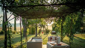 An outdoor seating area with wicker furniture under a pergola, overlooking a grassy field and a distant view. - Lovely holiday home in Val d’Orcia, with pool and large garden, near Pienza (Pienza)