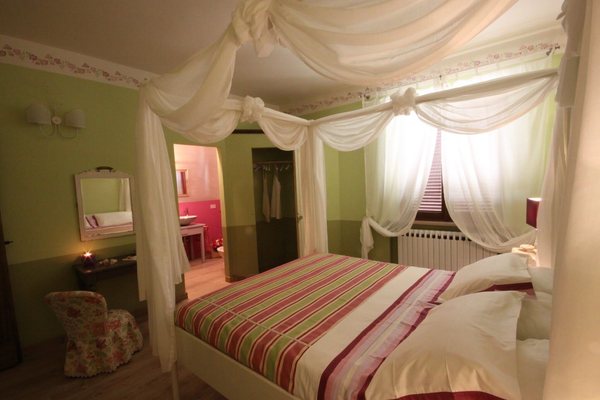 A bedroom with a canopy bed, a mirror, a vanity, and a chair.