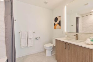 Bathroom features a toilet, vanity with mirror, and shower area with curtain.
