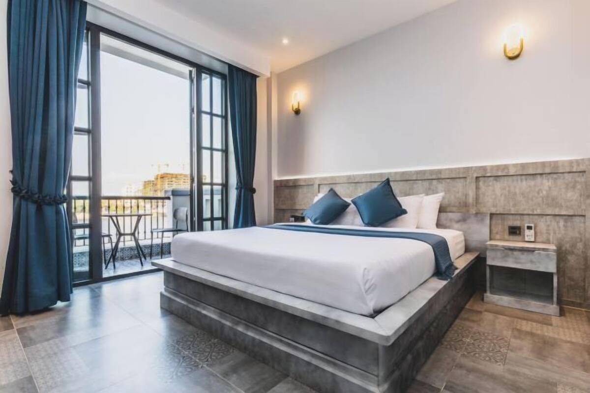 Een moderne hotelkamer met een groot bed, een klein nachtkastje en uitzicht op buiten.