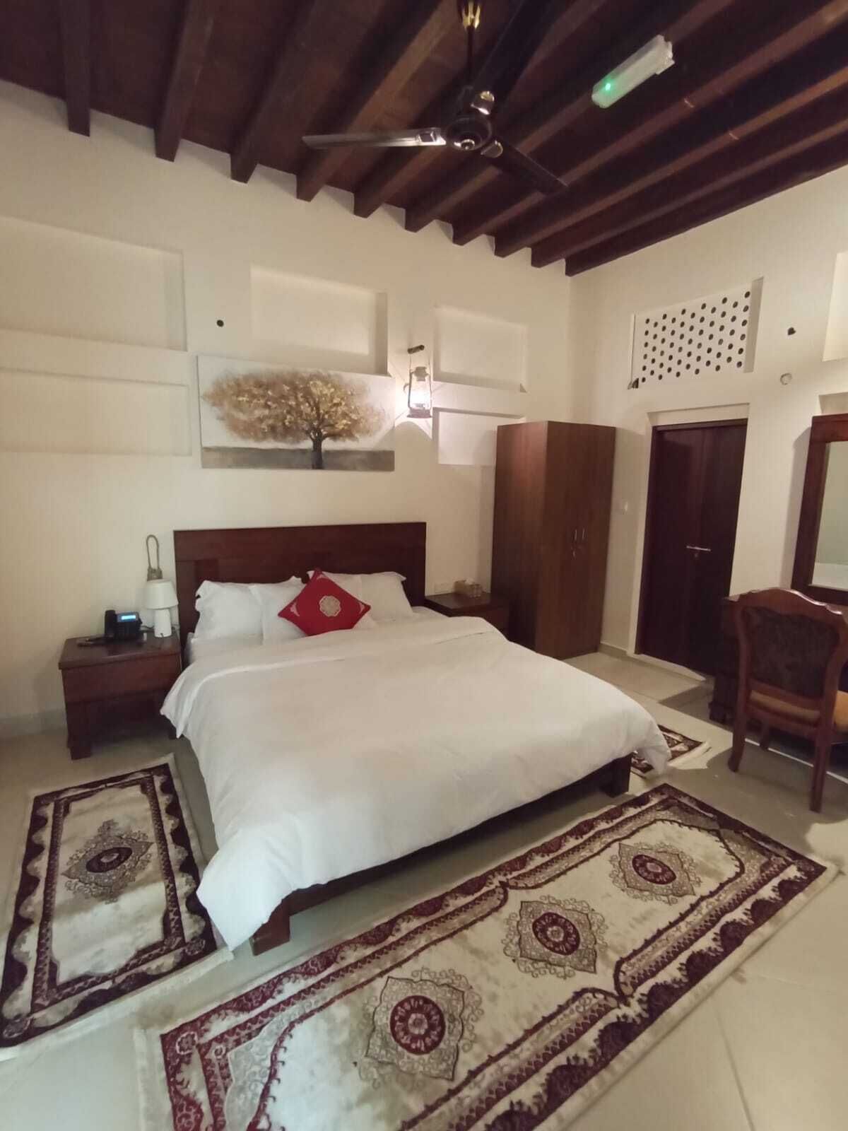 Un dormitorio con una cama grande, cabecera de madera, una mesita de noche con lámpara, una silla y un armario.