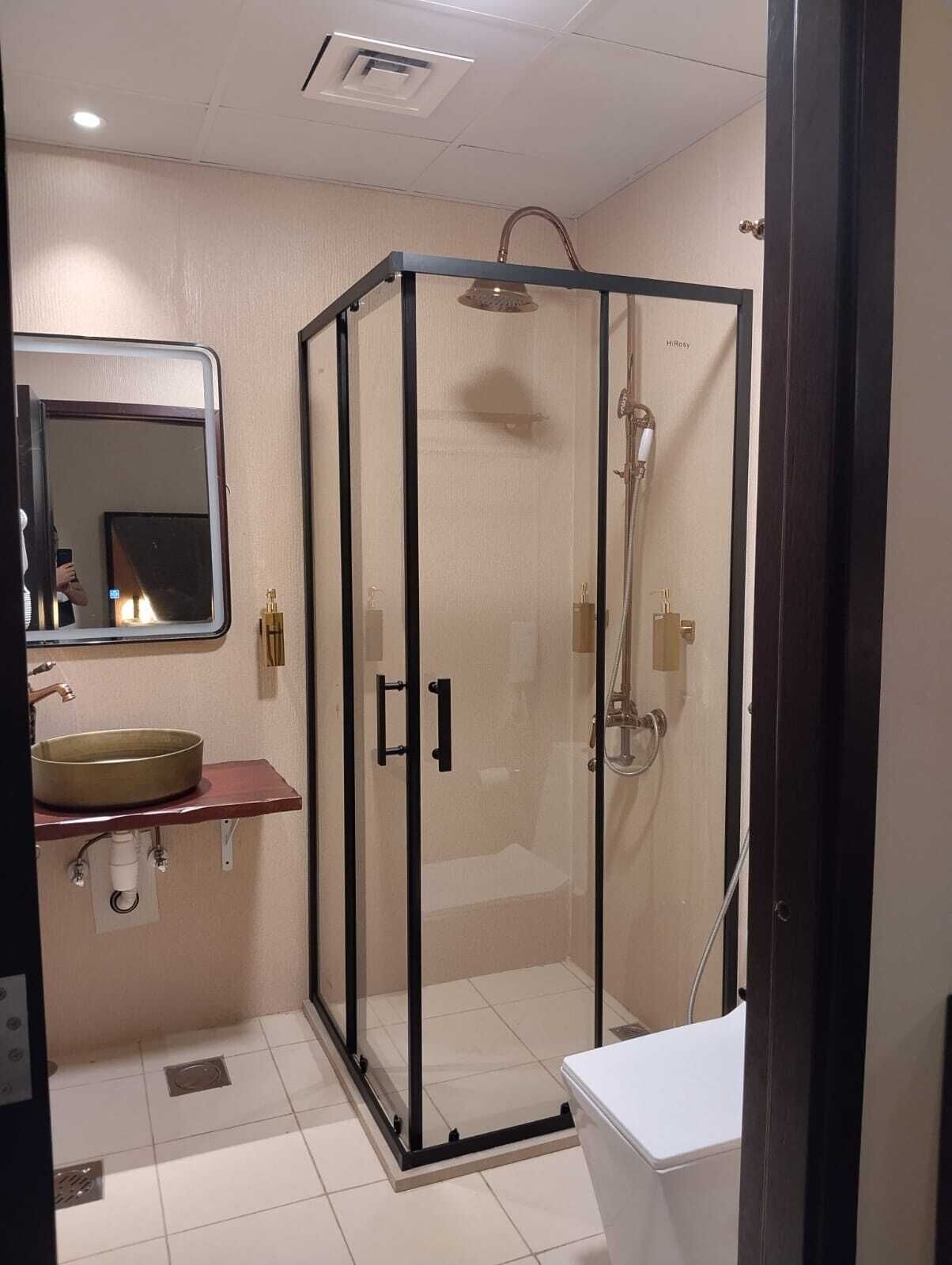 Un baño con cabina de ducha acristalada, un lavabo de porcelana color beige y un espejo sobre el lavabo.