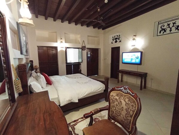 Une chambre à coucher avec un lit, une chaise en bois, un téléviseur et un ventilateur de plafond.