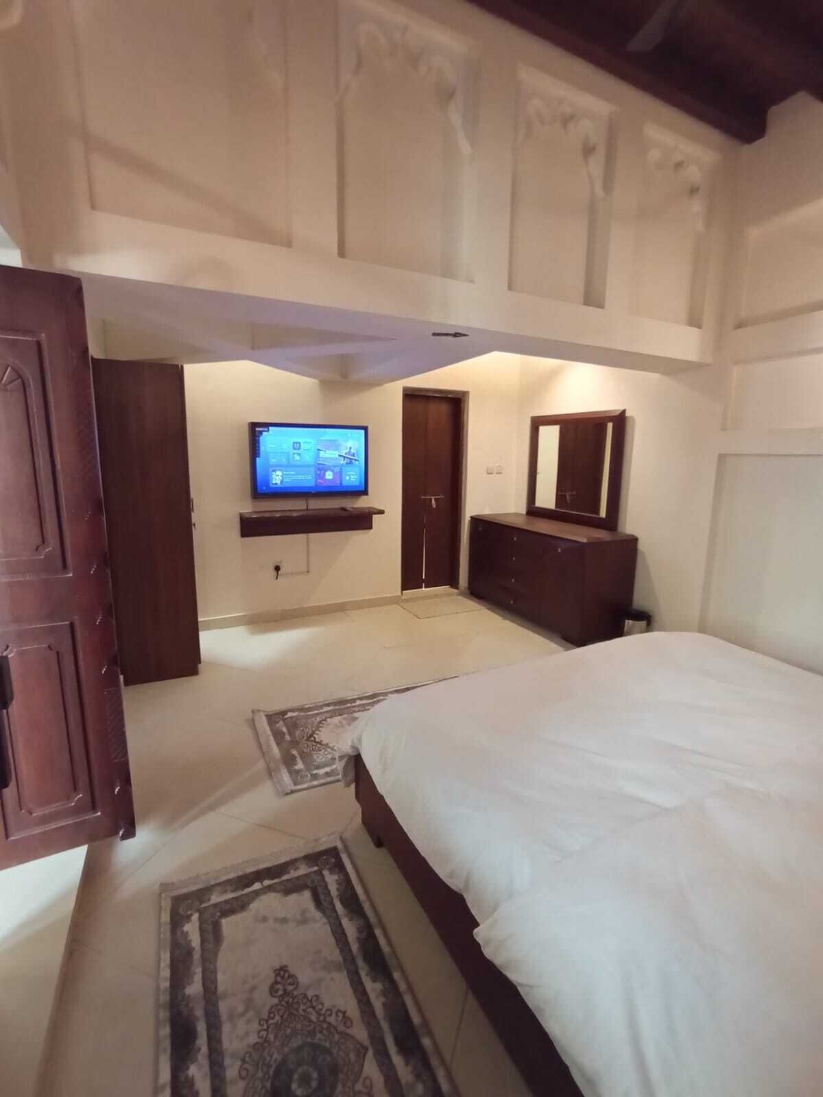 Een slaapkamer met een groot bed, een aan de muur bevestigde televisie, een dressoir en een deur.