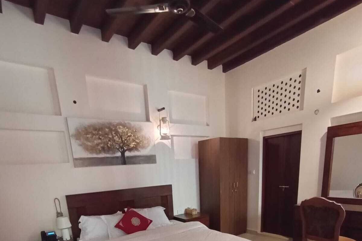 A bedroom with a large bed, wooden headboard, a nightstand, a wardrobe, a chair, and a mirror.