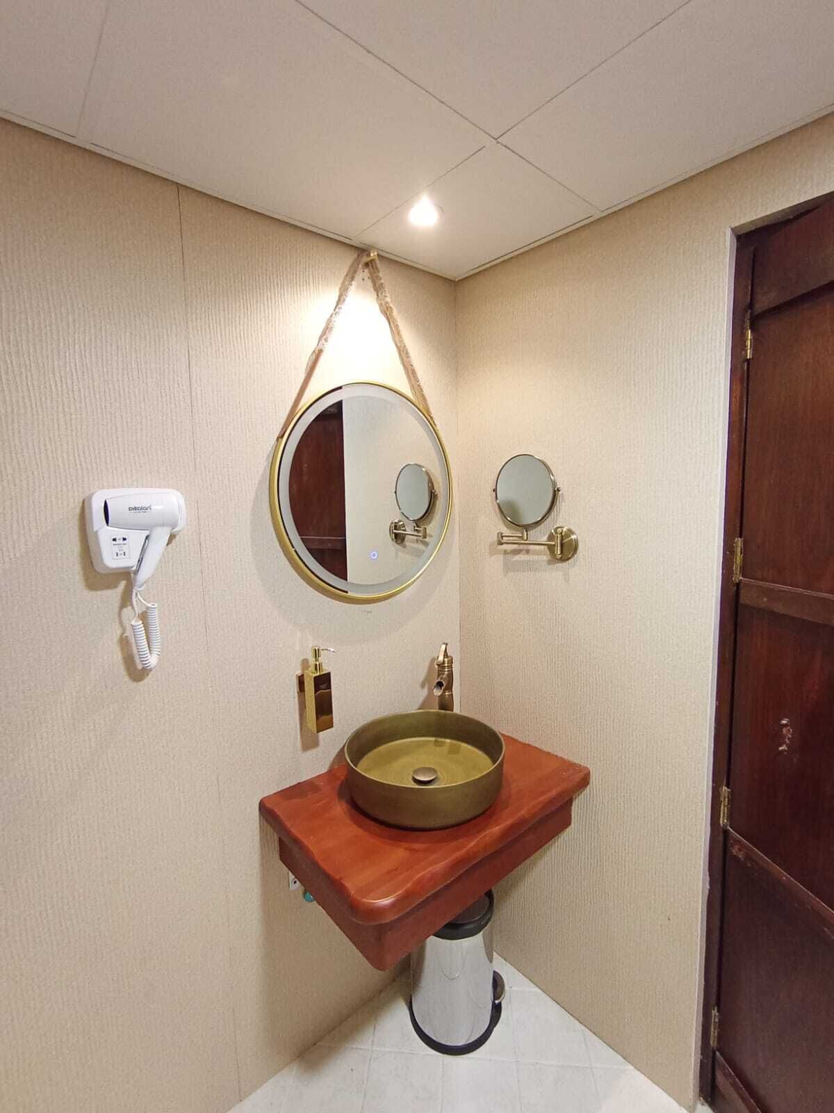 Ein Badezimmer mit einem Holzkosmetikschrank, einem runden Waschbecken, einem Spiegel und einem Fön an der Wand.
