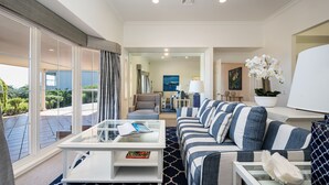 Une chambre d’hôtel moderne dotée d’un grand balcon, d’un ensemble de canapés, d’une table basse et offrant une vue sur l’extérieur.