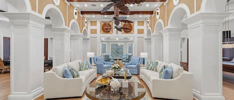 A spacious living room with a central glass coffee table, two sofas with patterned cushions, and a ceiling fan.