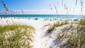 A sandy beach path leading to the ocean with beach umbrellas and people in the distance.