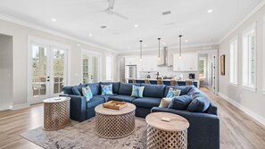 A spacious living room with a sectional sofa, round coffee tables, and a kitchen in the background.