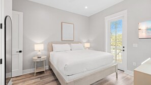 A bedroom with a bed, two bedside tables with lamps, a framed picture on the wall, and a window with a view.
