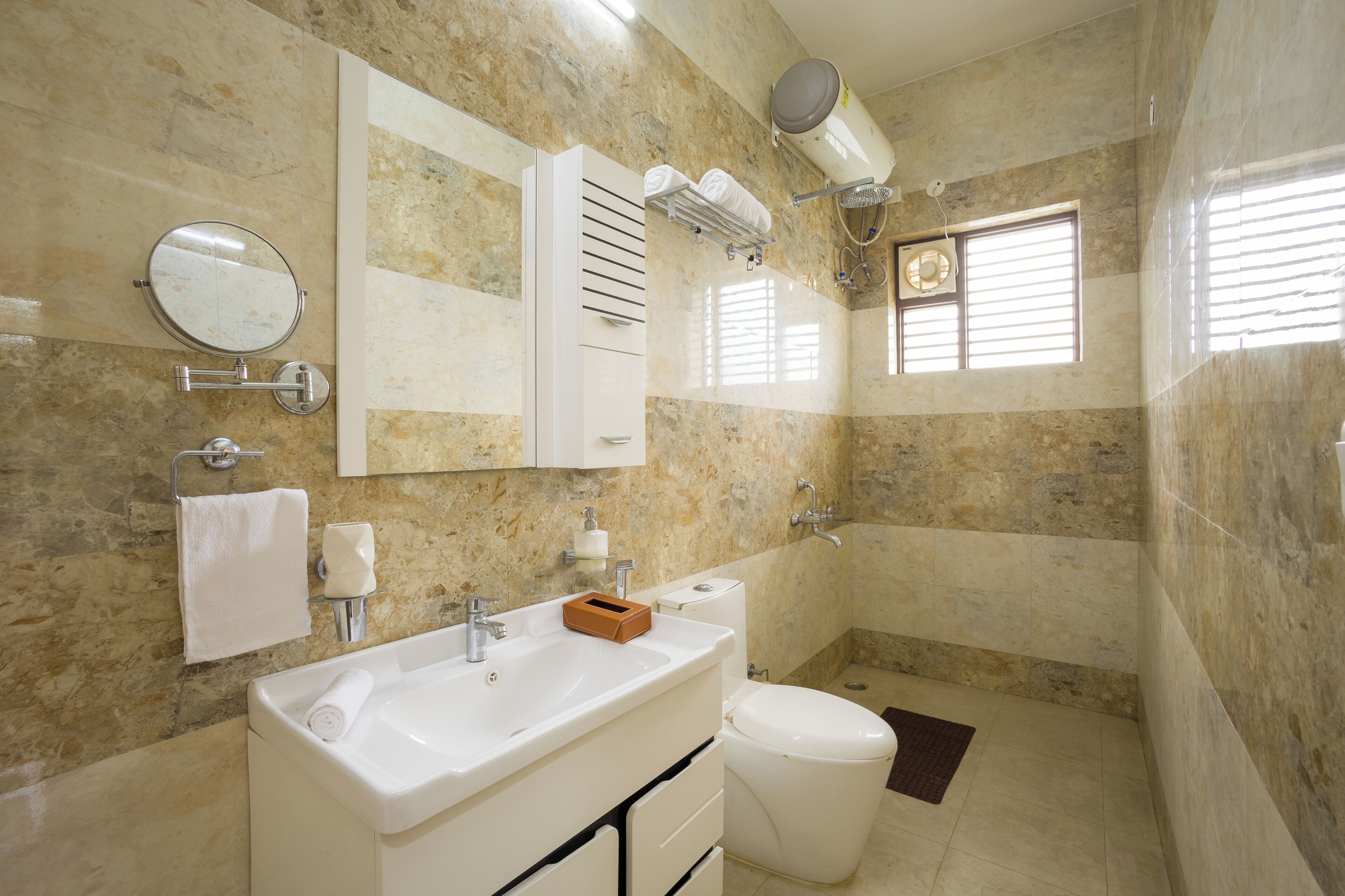Un baño con pared de mármol, un lavabo, un inodoro, un espejo y una ventana con persianas.