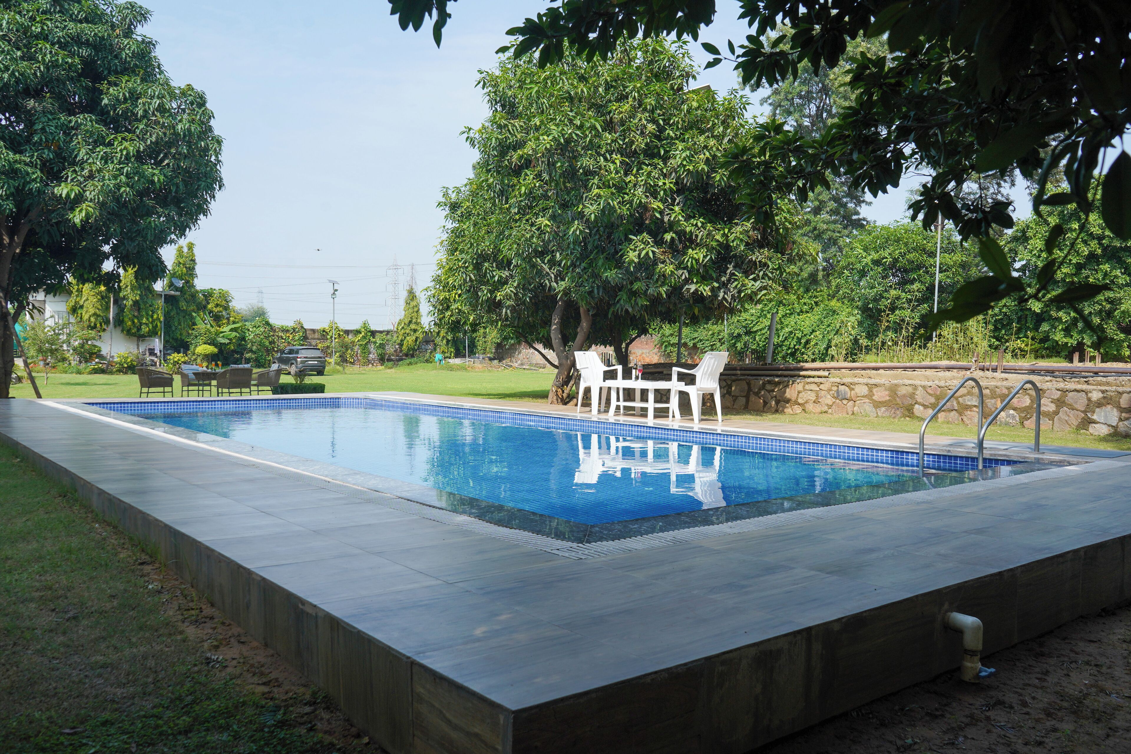 Une piscine rectangulaire bordée de carreaux, entourée d’un mur de pierre et d’une végétation luxuriante.