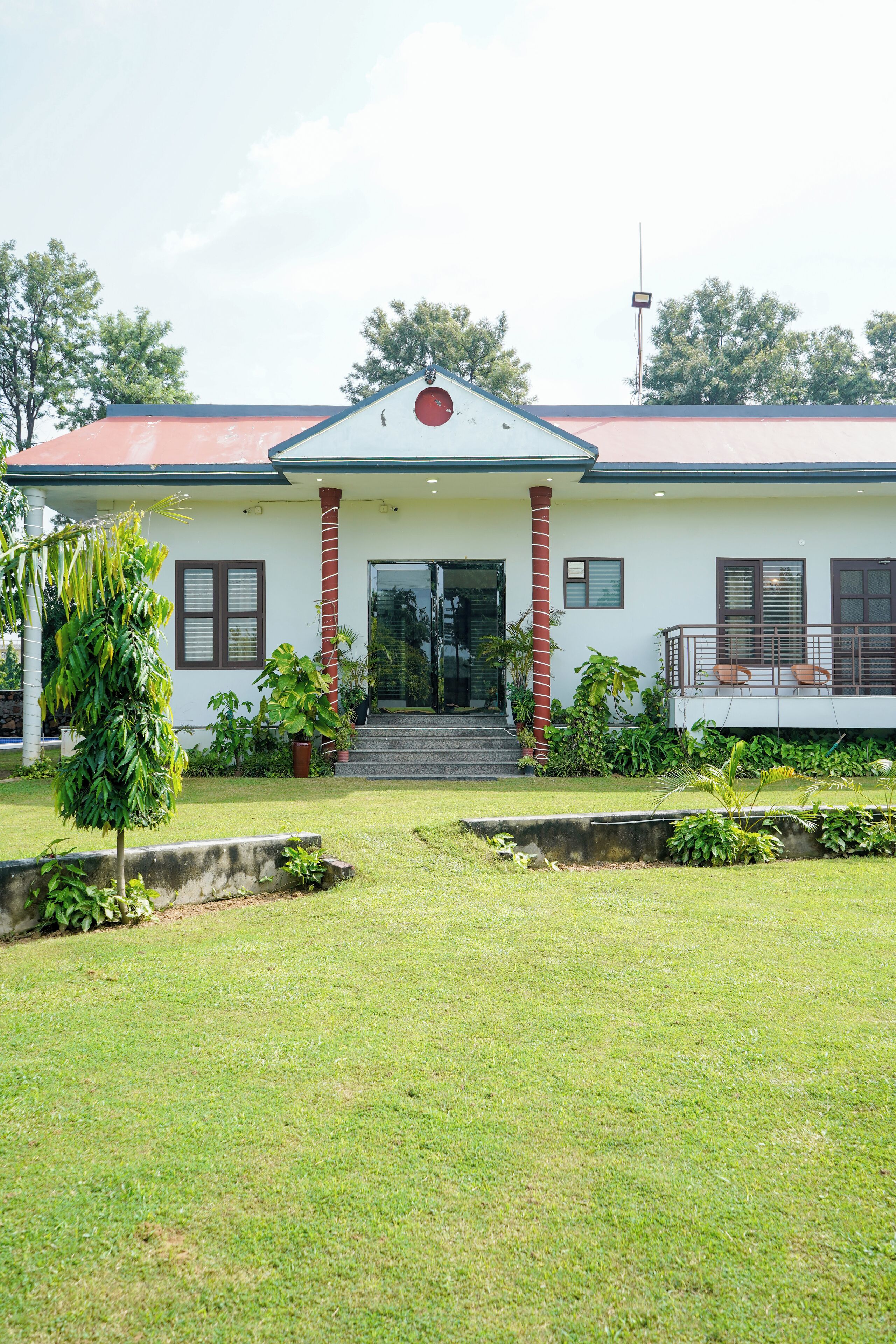 A two-story building with a red roof, a central entrance with steps, and a small porch with chairs.