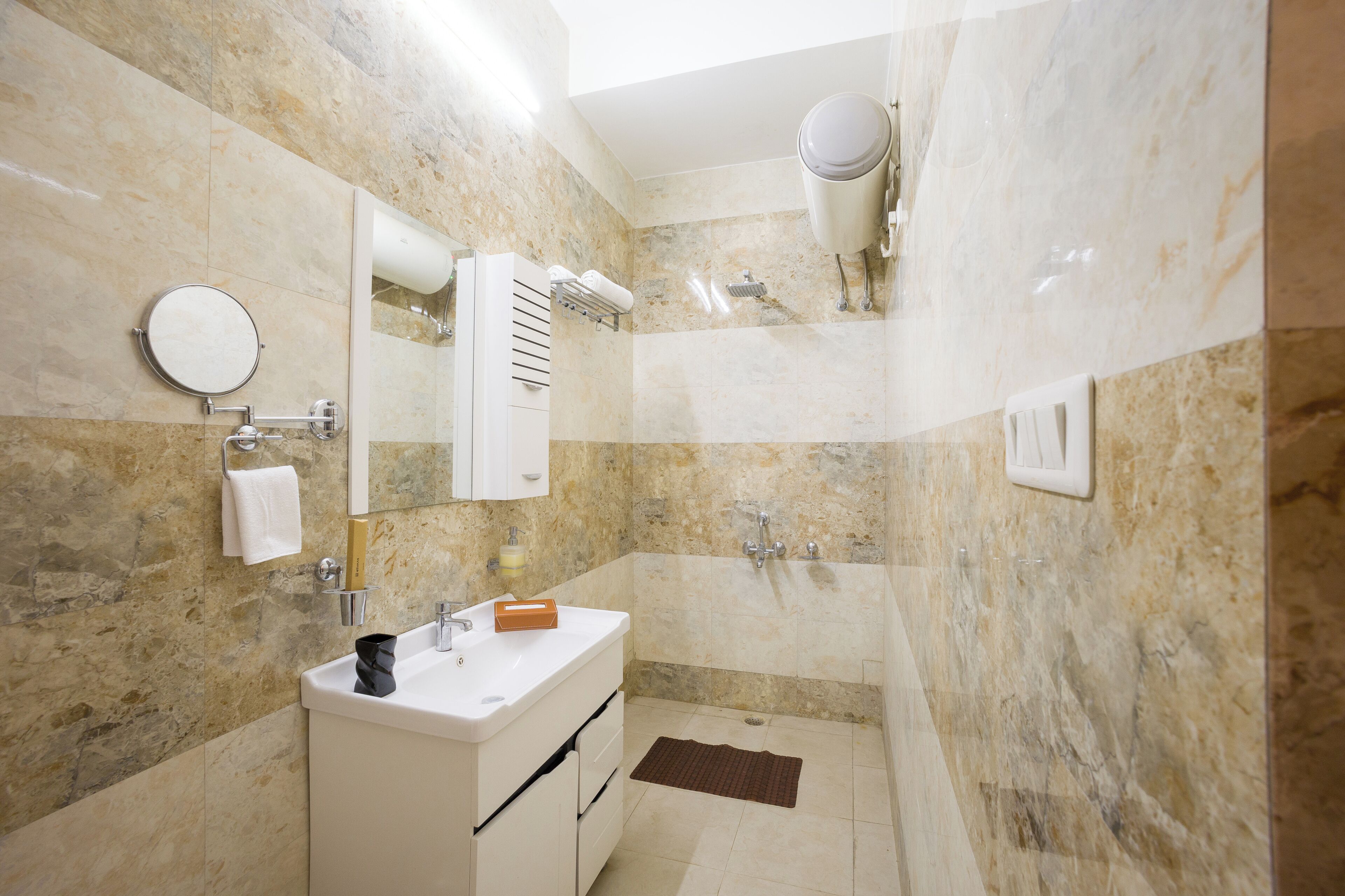 Un baño con pared de mármol, un lavamanos, un espejo, un perchero para toallas y una zona de ducha.