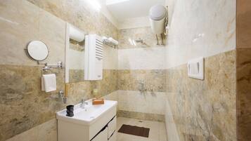 Un baño con pared de mármol, un lavamanos, un espejo, un perchero para toallas y una zona de ducha.