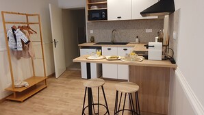 Une cuisine compacte équipée d’un four à micro-ondes, d’un évier et d’un petit réfrigérateur. On y trouve deux tabourets et une étagère en bois avec une tringle pour suspendre les vêtements.