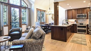 Amplia sala de estar con un sofá grande, una mesa de comedor y una cocina con armarios de madera y electrodomésticos de acero inoxidable.