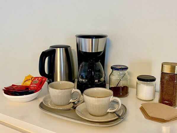A tray with two cups, a coffee maker, a jar of sugar, a jar of spices, and packets of tea.