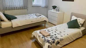 A bedroom with two beds, a dresser, a radiator, a window with curtains, and a painting on the wall. - Cozy room in Remich (Remich)