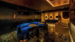 A modern lounge area with a curved blue sofa, round tables, and a patterned floor. - Hotel Malika Residency (Ettumanoor)
