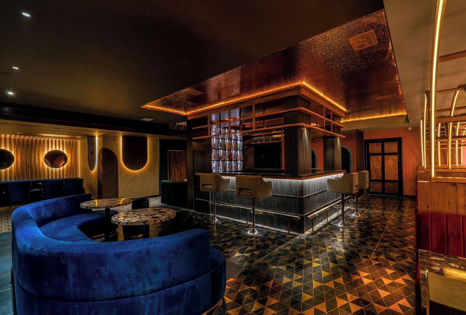A modern bar area with a bar counter, seating, and a patterned floor.