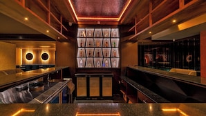 A bar area with a central display of liquor bottles, wooden ceiling beams, and a modern bar counter. - Hotel Malika Residency (Ettumanoor)