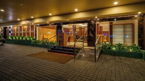 A hotel entrance with a marble facade, a reception desk, and a staircase leading to the lobby. - Hotel Malika Residency (Ettumanoor)