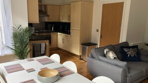 Un espacio habitable compacto con comedor, kitchenette y un sofá gris con almohadones decorativos.