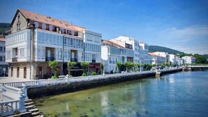 A waterfront hotel with multiple floors, a river in the foreground, and a bridge connecting to the opposite bank. - The Cliffs - Vue de Pantin (Valdoviño)