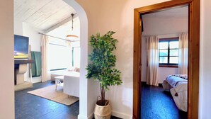 A room with a bed, a window with curtains, a plant in a woven basket, and a television in the corner. - The Cliffs - Vue de Pantin (Valdoviño)