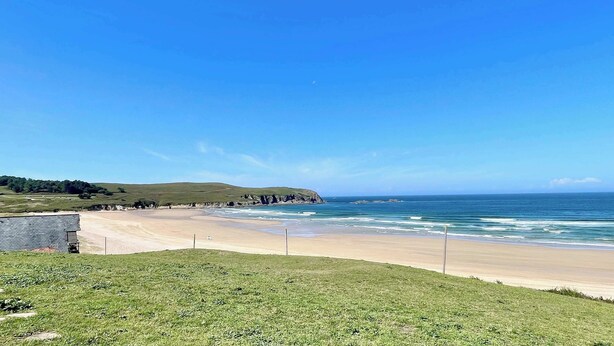A beach with a grassy area in the foreground, a sandy beach, and a view of the ocean. - The Cliffs - Vue de Pantin (Valdoviño)