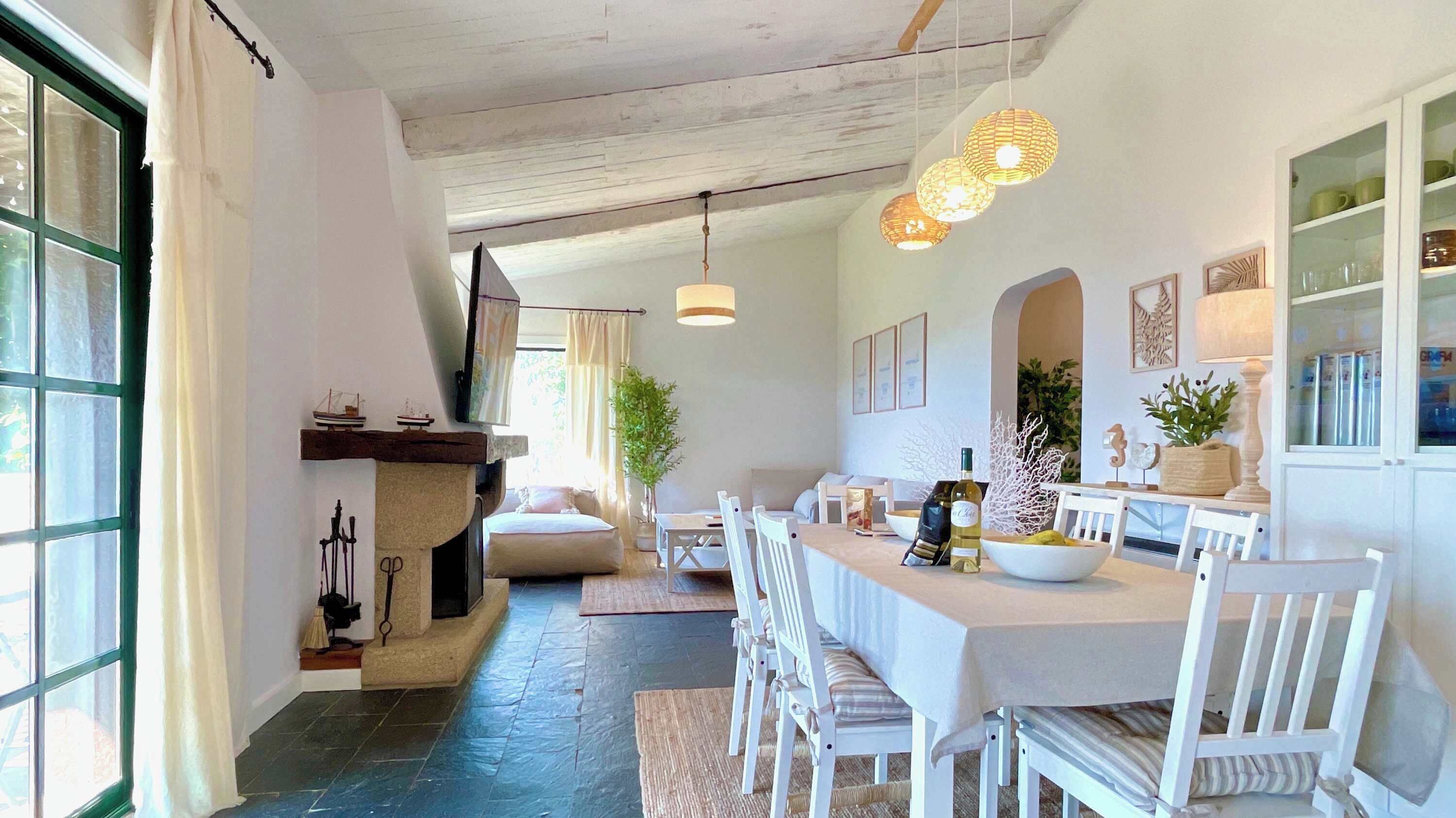 Un vaste espace dédié à la salle à manger, avec une longue table, des chaises blanches et des luminaires suspendus.