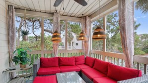 A covered outdoor seating area with a red sofa, hanging lamps, and a view of a house in the background.