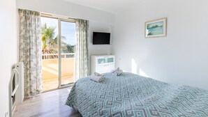 Une chambre avec une couvre-lit à motifs, un téléviseur à écran plat fixé au mur, une petite table de chevet et une fenêtre avec des rideaux.