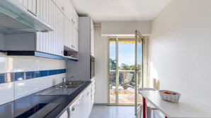 Une cuisine moderne avec des meubles blancs, un plan de travail noir et une porte-fenêtre coulissante donnant sur un espace de détente extérieur.