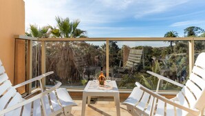 Un balcon avec deux chaises blanches, une petite table et une bouteille de spiritueux.